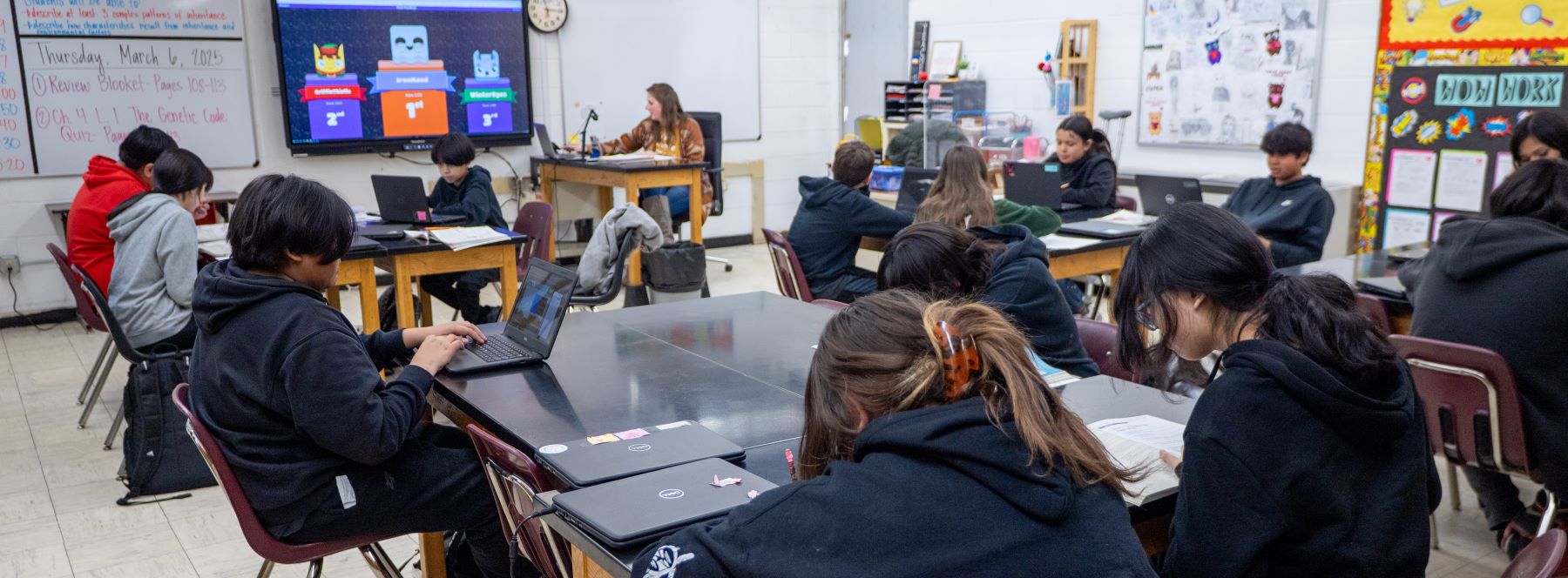 A teacher guides students in a classroom, where they are focused on their laptops during a lesson.