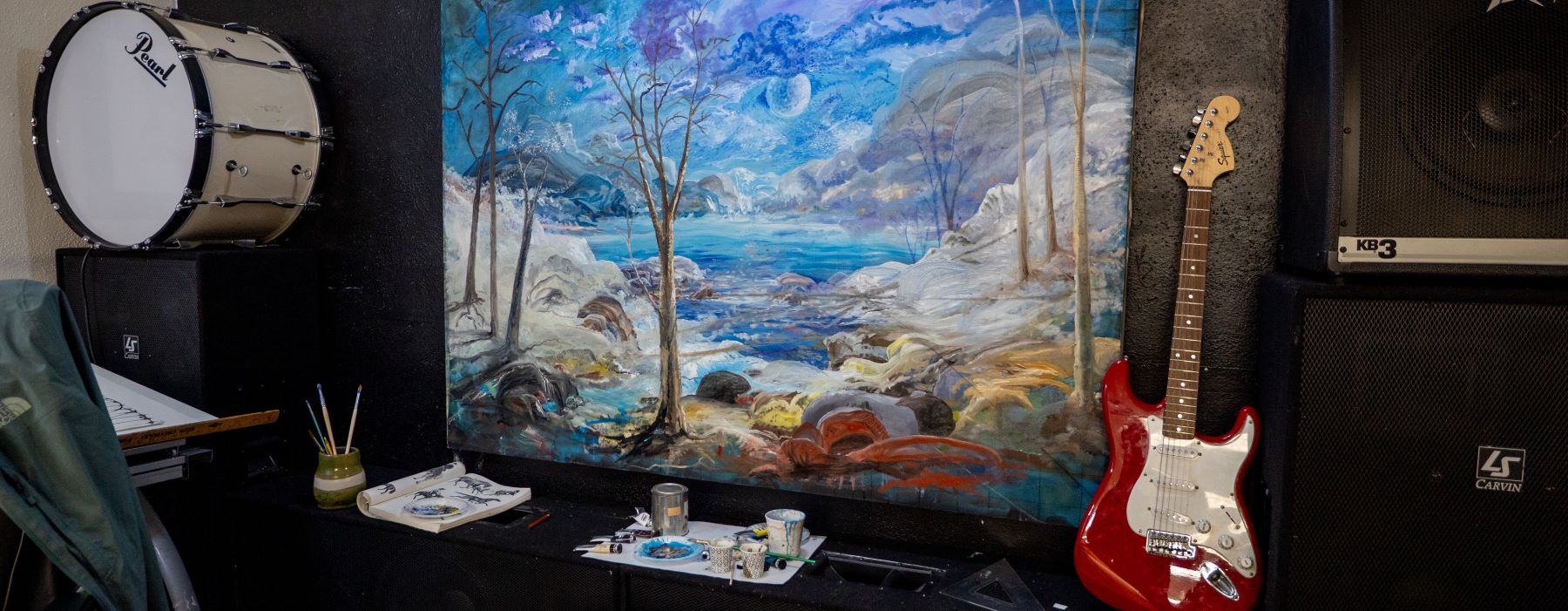 A mountain painting hangs on the wall, surrounded by various musical instruments, creating a cozy artistic space.