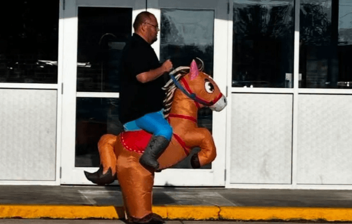 A man rides an inflatable orange horse costume outside a building.