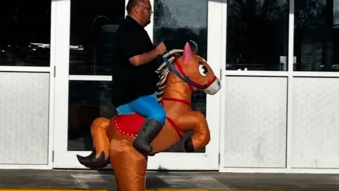 A man rides an inflatable orange horse costume outside a building.