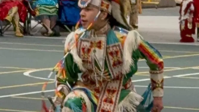 Student dressed in regalia and dancing in the center of the gym