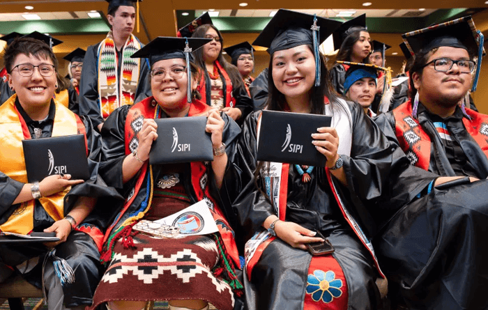 Students wearing caps and gowns while holding their diploma.