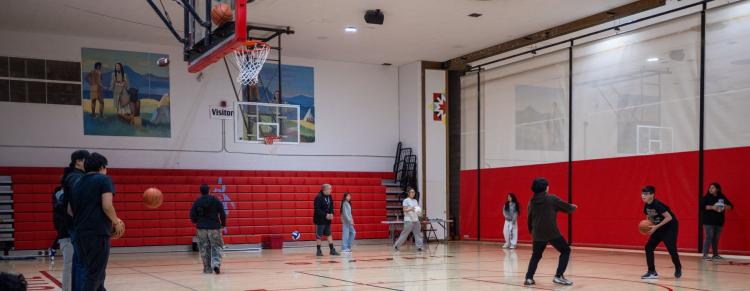 Several players are engaged in a basketball game inside a gym, with one shooting while others are ready to pass.