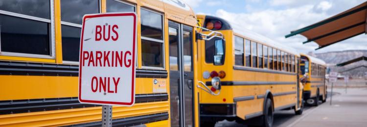School buses parked in a line next to a bus parking only sign waiting for students to board.